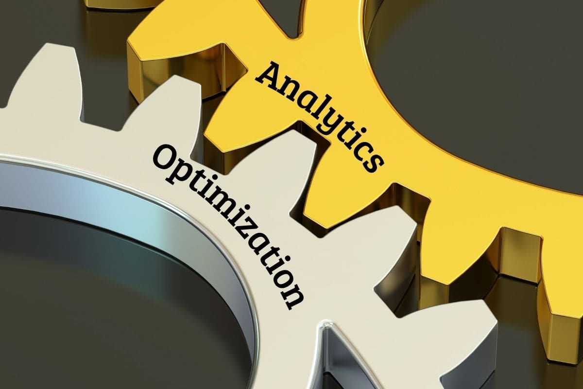 Zwei ineinandergreifende Zahnräder, eines goldfarben mit dem Wort „Analytics“ und eines silberfarben mit dem Wort „Optimization“, symbolisieren die Zusammenarbeit von Analyse und Optimierung.