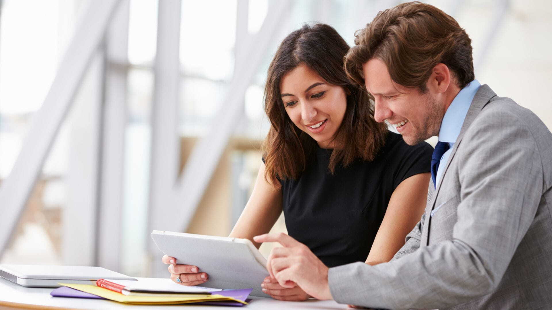 Ein Mann und eine Frau schauen gemeinsam auf ein Tablet, während sie Inhalte für einen Unternehmensblog besprechen.