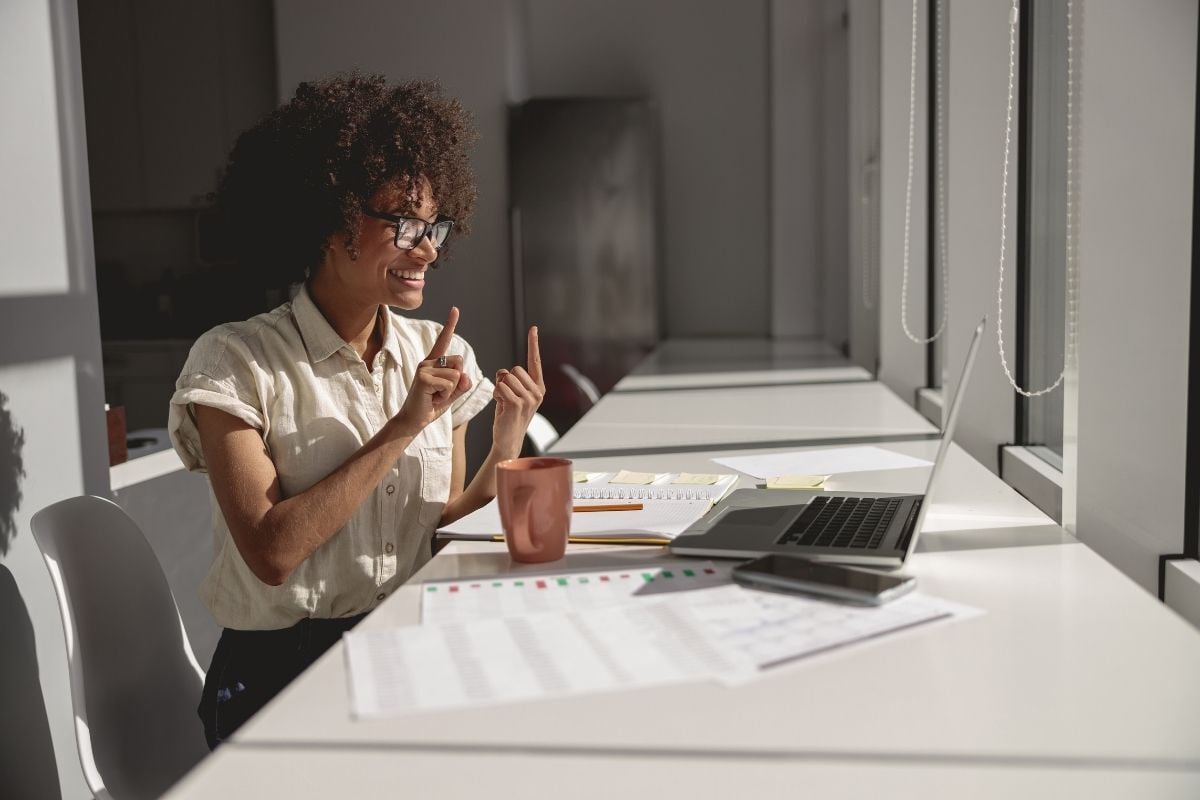 Person, die mit ihrer Community an einem langen weißen Tisch in einem modernen Büro mit Laptop, Dokumenten und Tageslicht kommuniziert – einschließlich barrierefreier Kommunikation im digitalen Marketing.