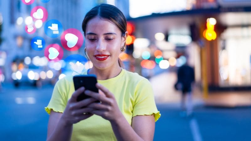 Frau, die in einer von Stadtlichtern beleuchteten Straße auf ihrem Handy soziale Medien checkt.