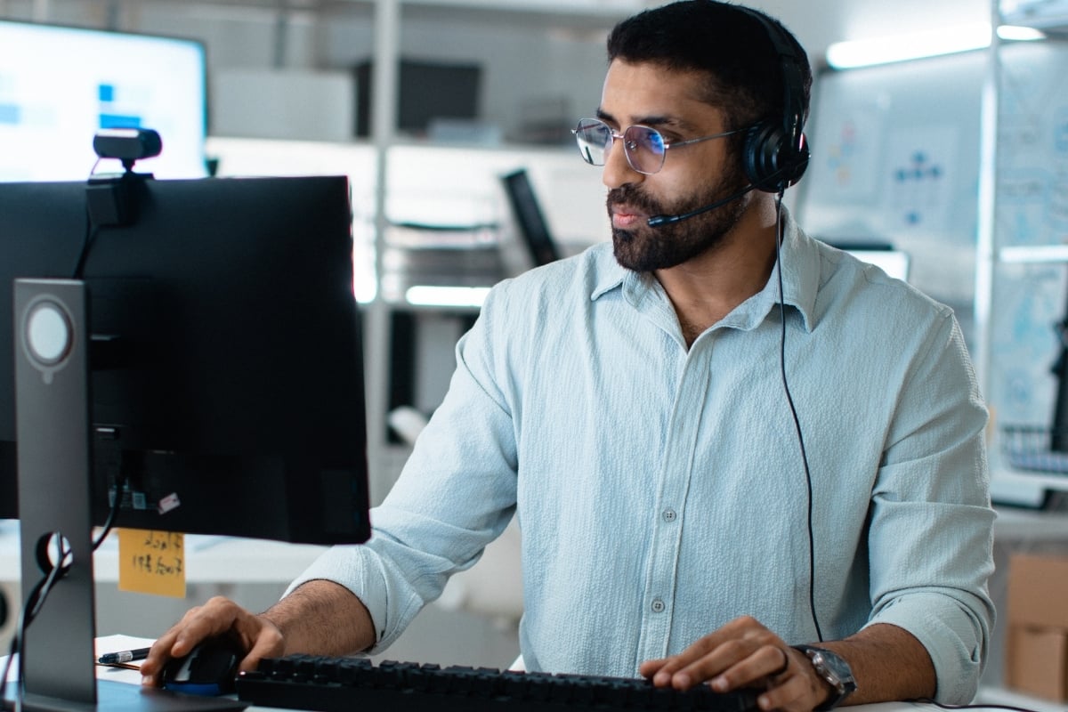Profissional de suporte técnico com headset atendendo em frente a múltiplos monitores em um escritório.