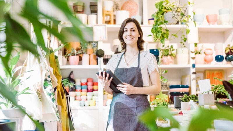 Floristin mit Tablet im Laden, umgeben von Pflanzen – digitale Geschäftsführung im Einzelhandel mit Fokus auf Kundenservice.