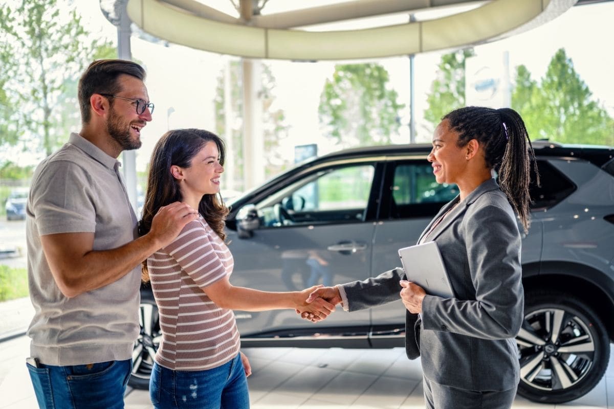 Zwei Kunden geben einer Verkäuferin im Autohaus die Hand, Symbol für den erfolgreichen Abschluss im Inbound-Marketing
