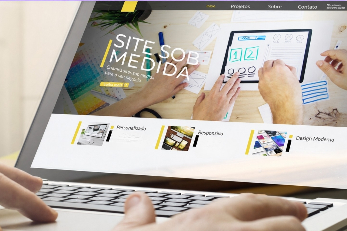 Laptop sobre mesa de madeira exibindo a tela inicial de um site personalizado, com menu de navegação e cards de destaque, enquanto duas mãos digitam no teclado.