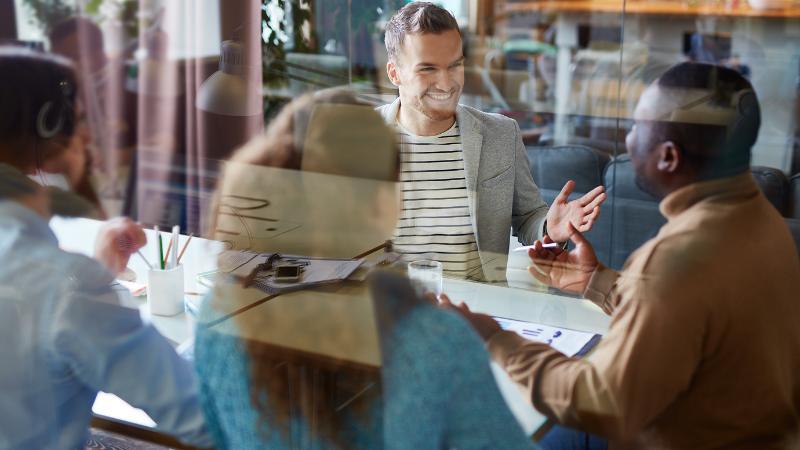 Team-Meeting in einem modernen Büro, bei dem Kollegen an einem Tisch diskutieren und Dokumente durchsehen.