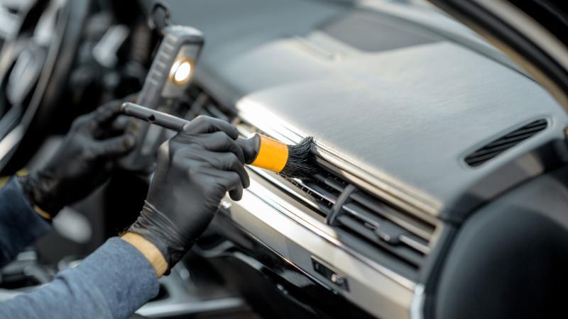 Person reinigt Auto-Lüftung mit Pinsel und Handschuhen – Detailarbeit für Sauberkeit im Fahrzeuginnenraum.